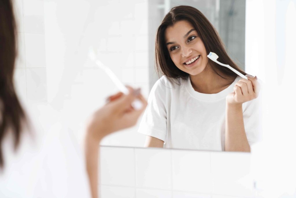 Woman brushing teeth with a smile in a bathroom mirror